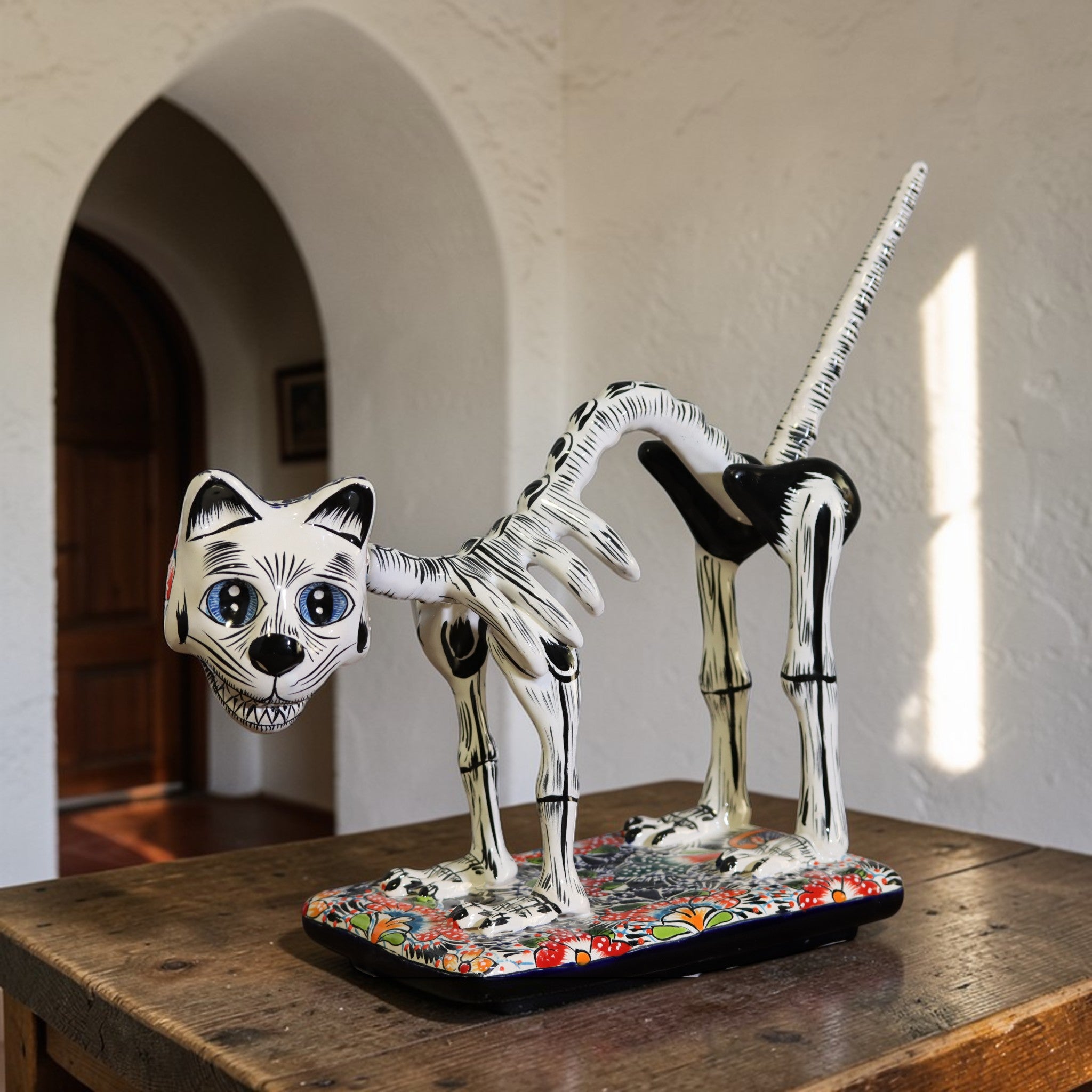 Hand painted Talavera skeletal cat sculpture on colorful base styled in a white hacienda interior setting