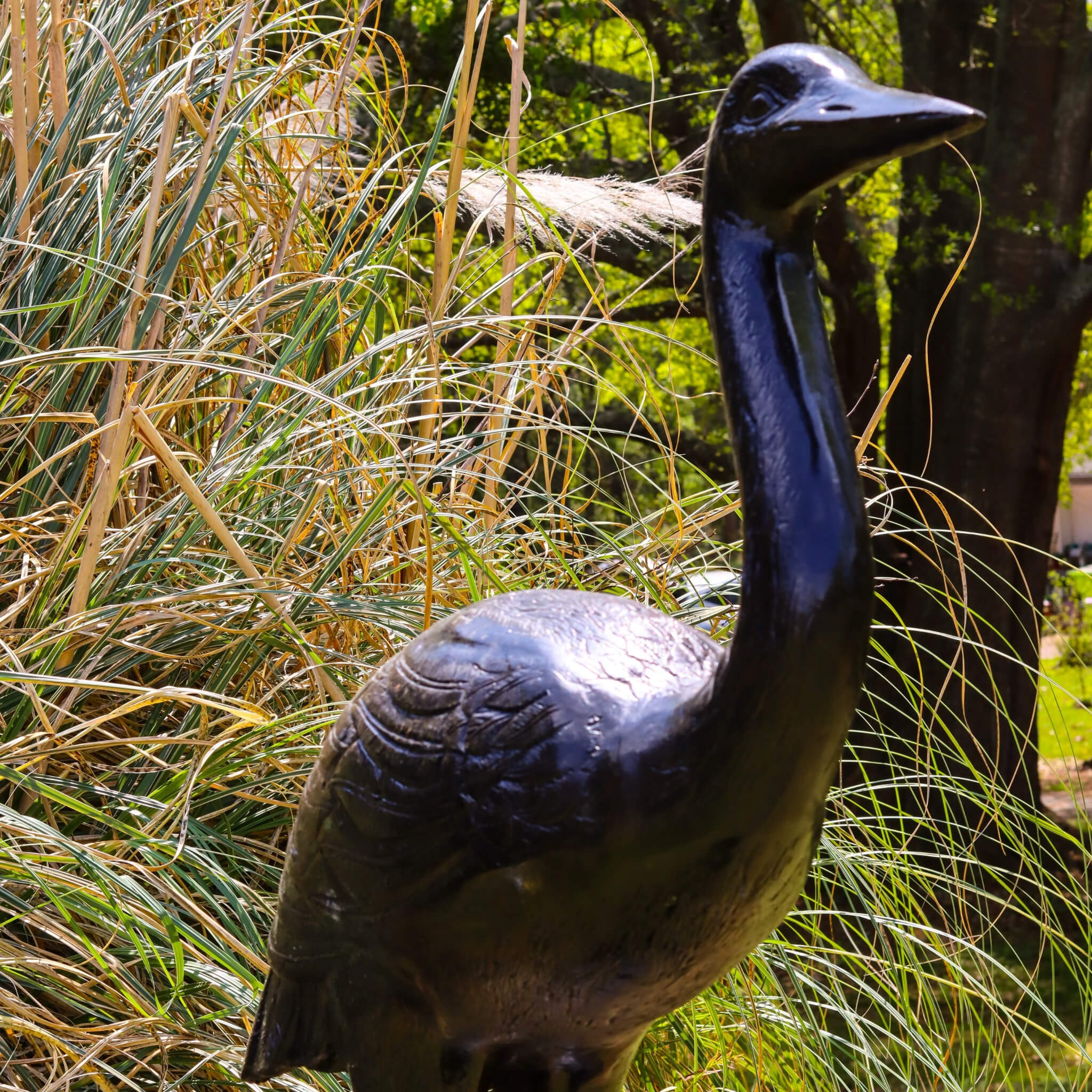 Close up of cast aluminum heron sculpture body showing detailed feather texture and dark patina finish in garden grass setting