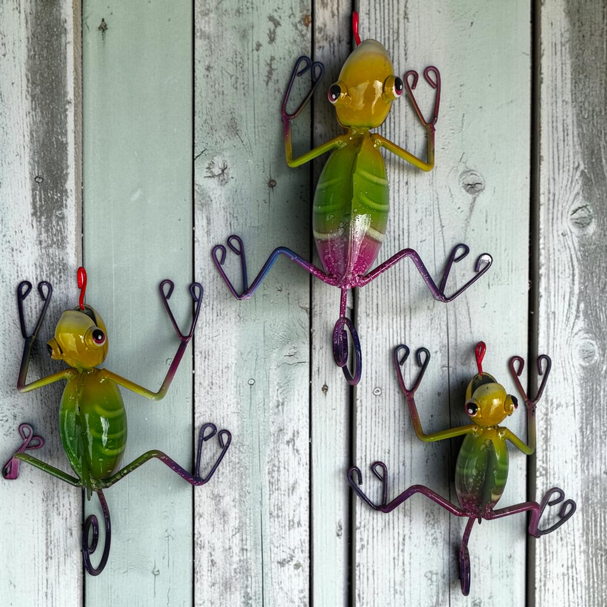 Three hand-painted Mexican folk art metal climbing lizards in green and yellow on pale teal weathered wood plank wall, Jalisco wall décor