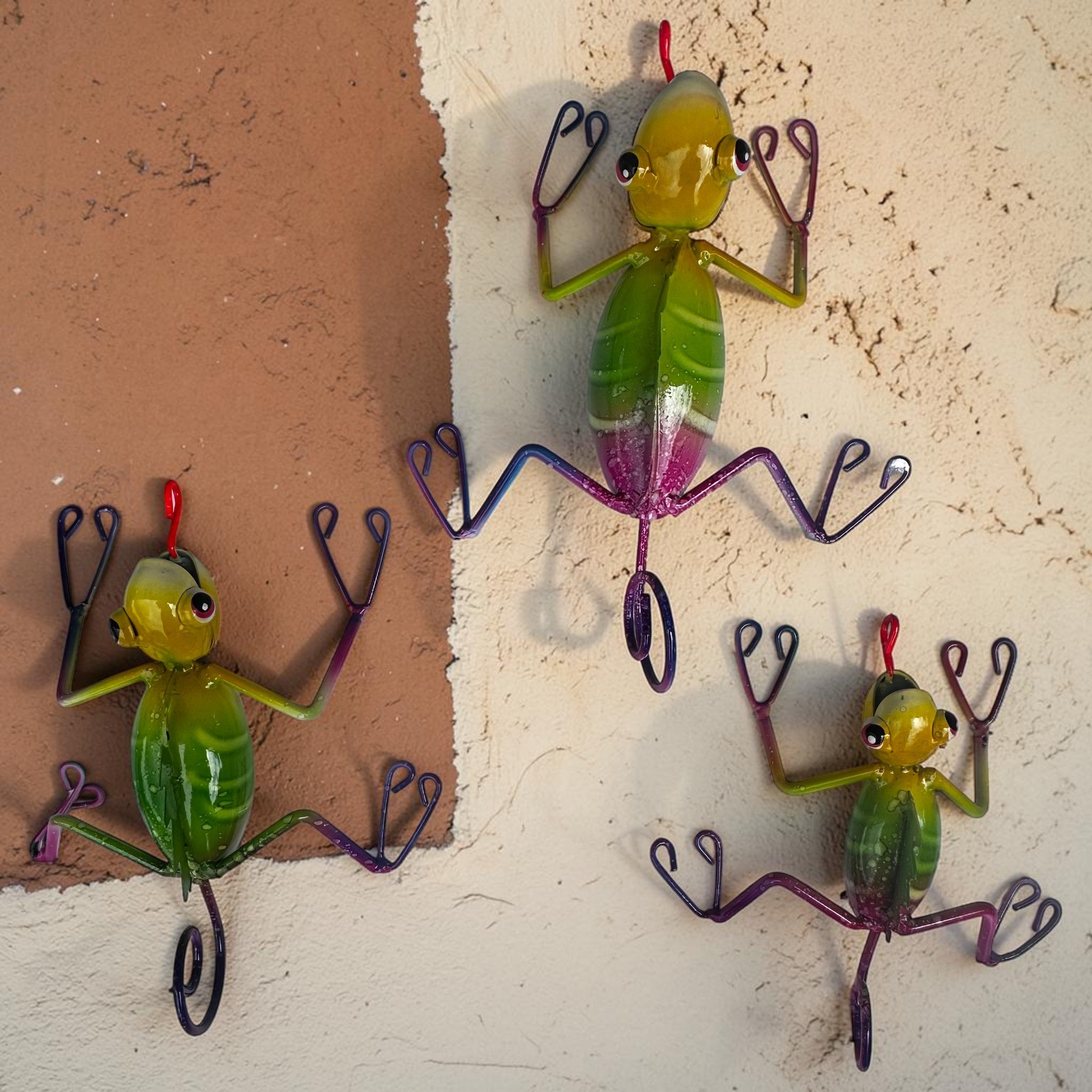 Mexican folk art climbing lizards mounted on warm terracotta wall, hand-painted set of 3 green geckos with iridescent pink legs