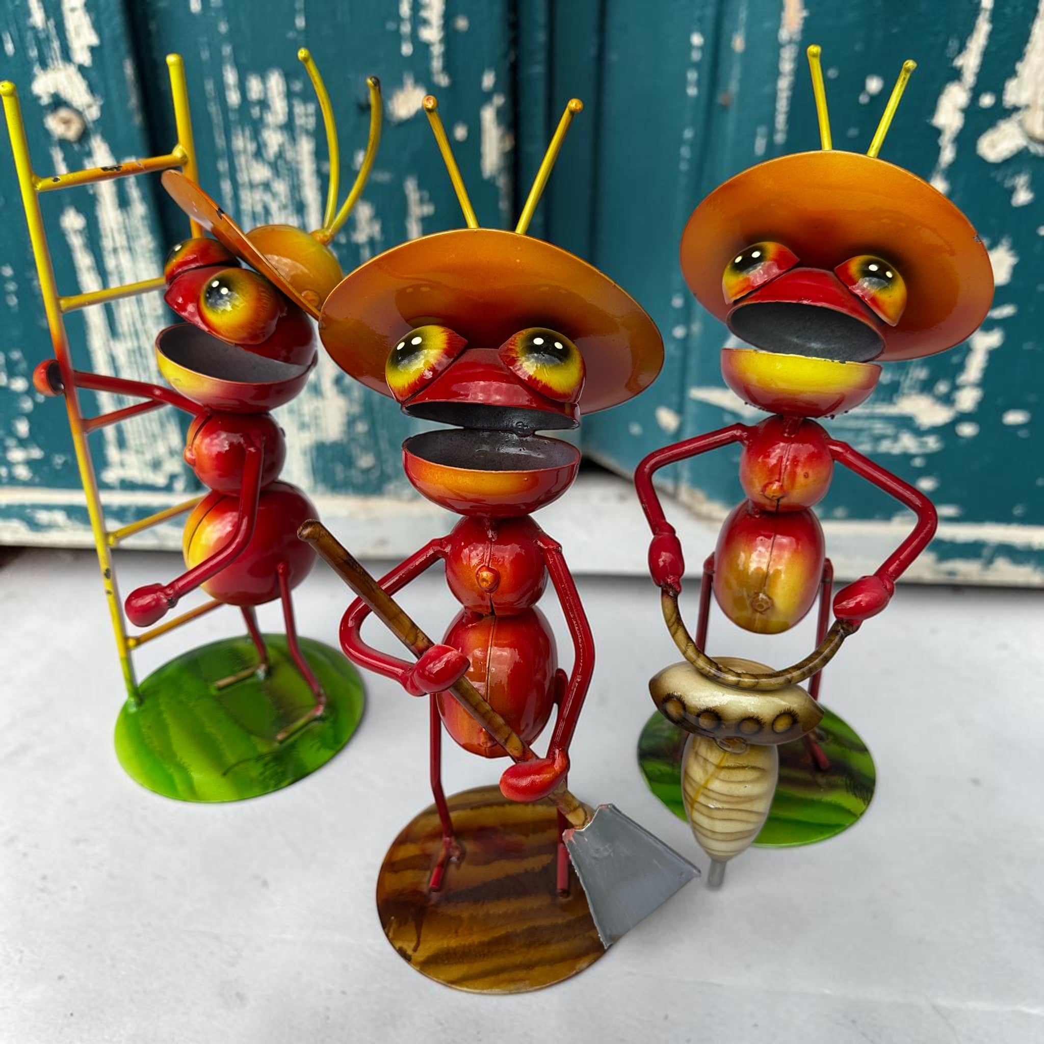 Whimsical Mexican folk art ant figurines in red and yellow with traditional sombreros, each carrying a different work tool