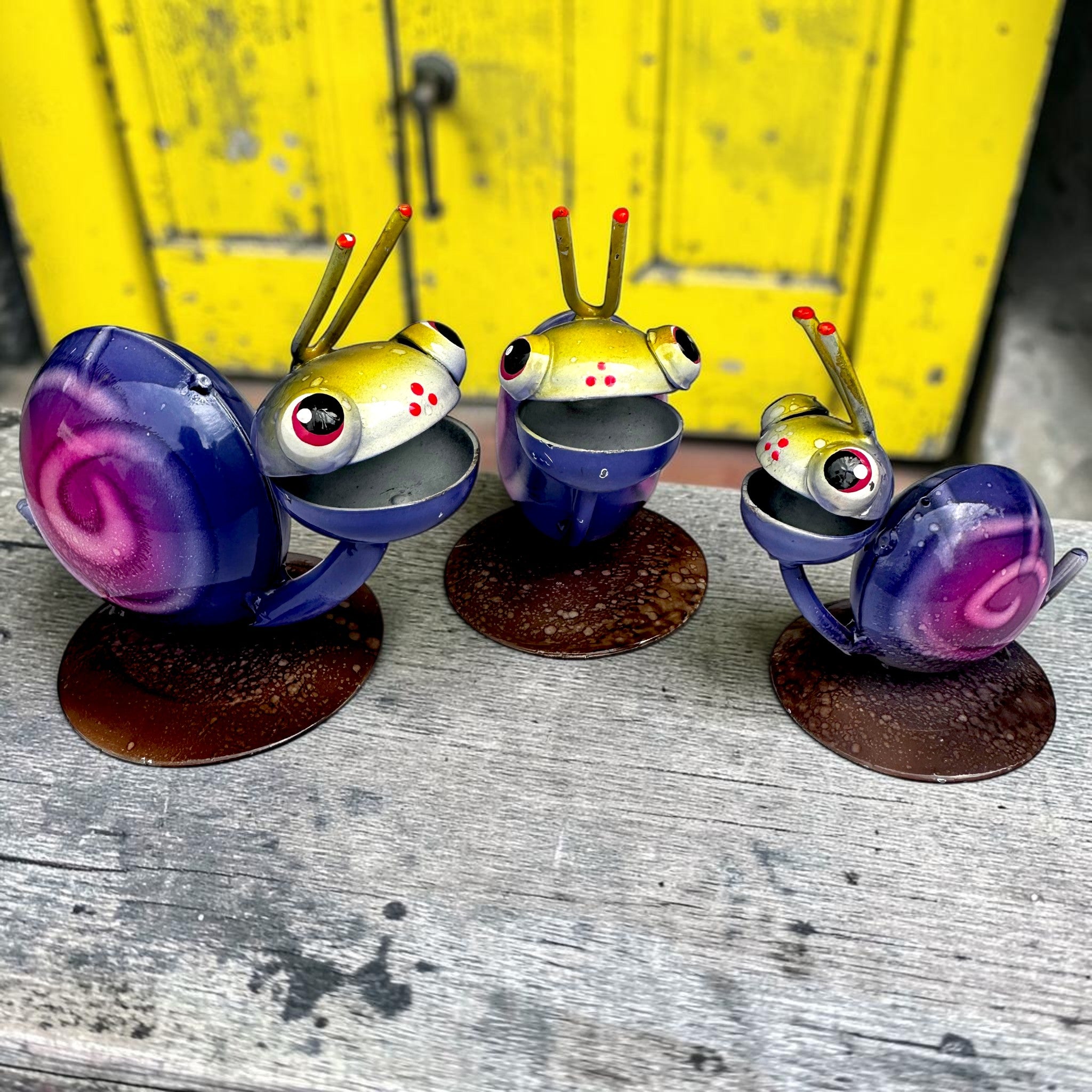 Set of three hand-painted metal snail sculptures from Jalisco Mexico with hot pink swirl shells and warm yellow heads, whimsical garden décor