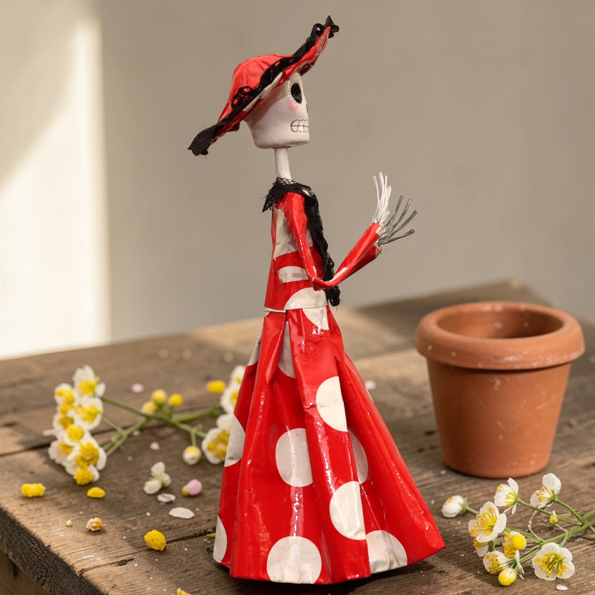 Side view of red polka dot Catrina figurine with delicate metal skeletal hands holding a bouquet, Mexican papier-mâché folk art