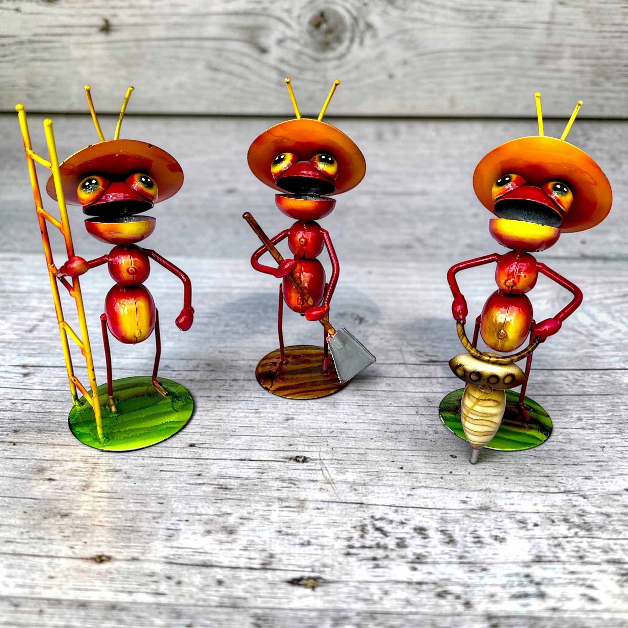 Whimsical Mexican folk art ant figurines in red and yellow with traditional sombreros, each carrying a different work tool