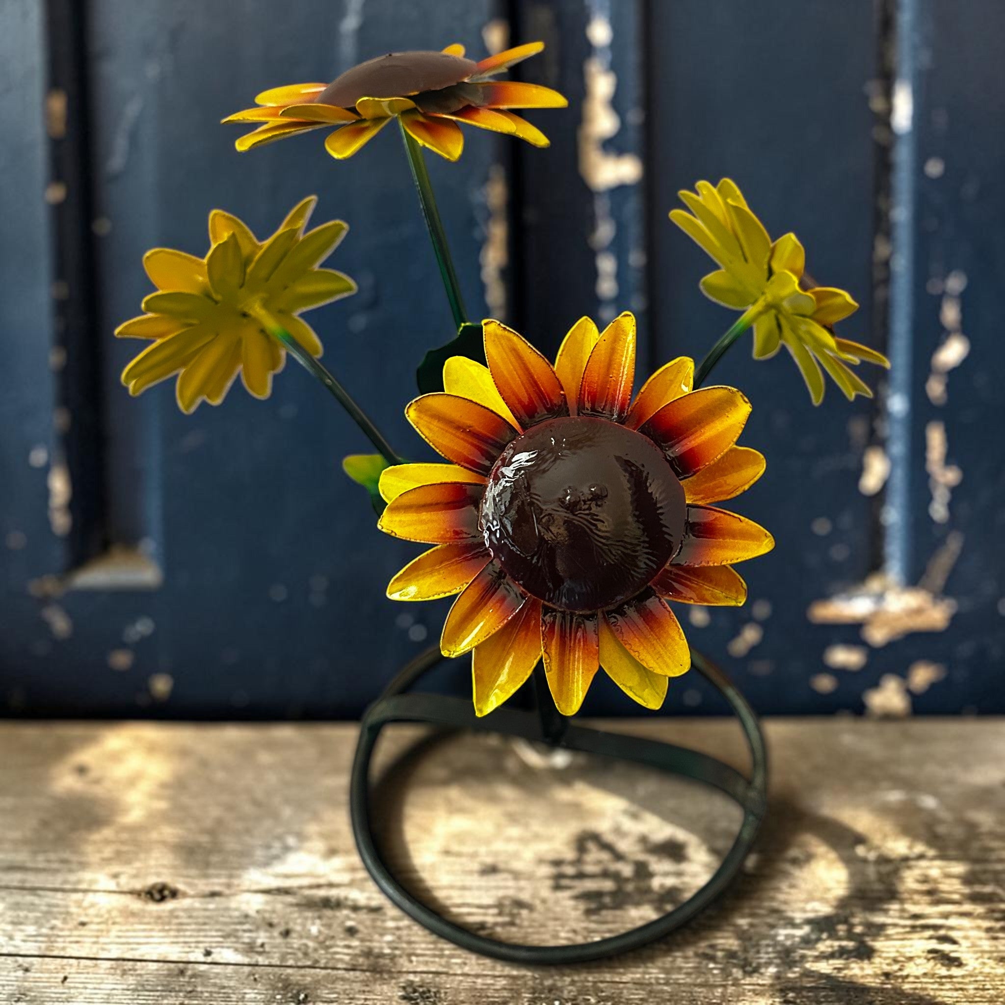 Close detail of hand-painted metal sunflower yard art with multiple bloom heads on wire stand, rustic Mexican folk art outdoor decor