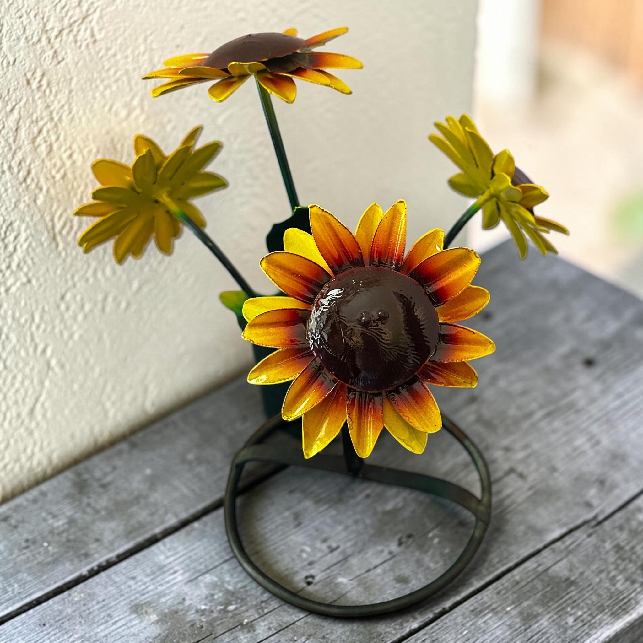 Hand-painted sunflower garden sculpture on weathered wood with soft cream stucco wall behind, minimalist yard art and patio decor