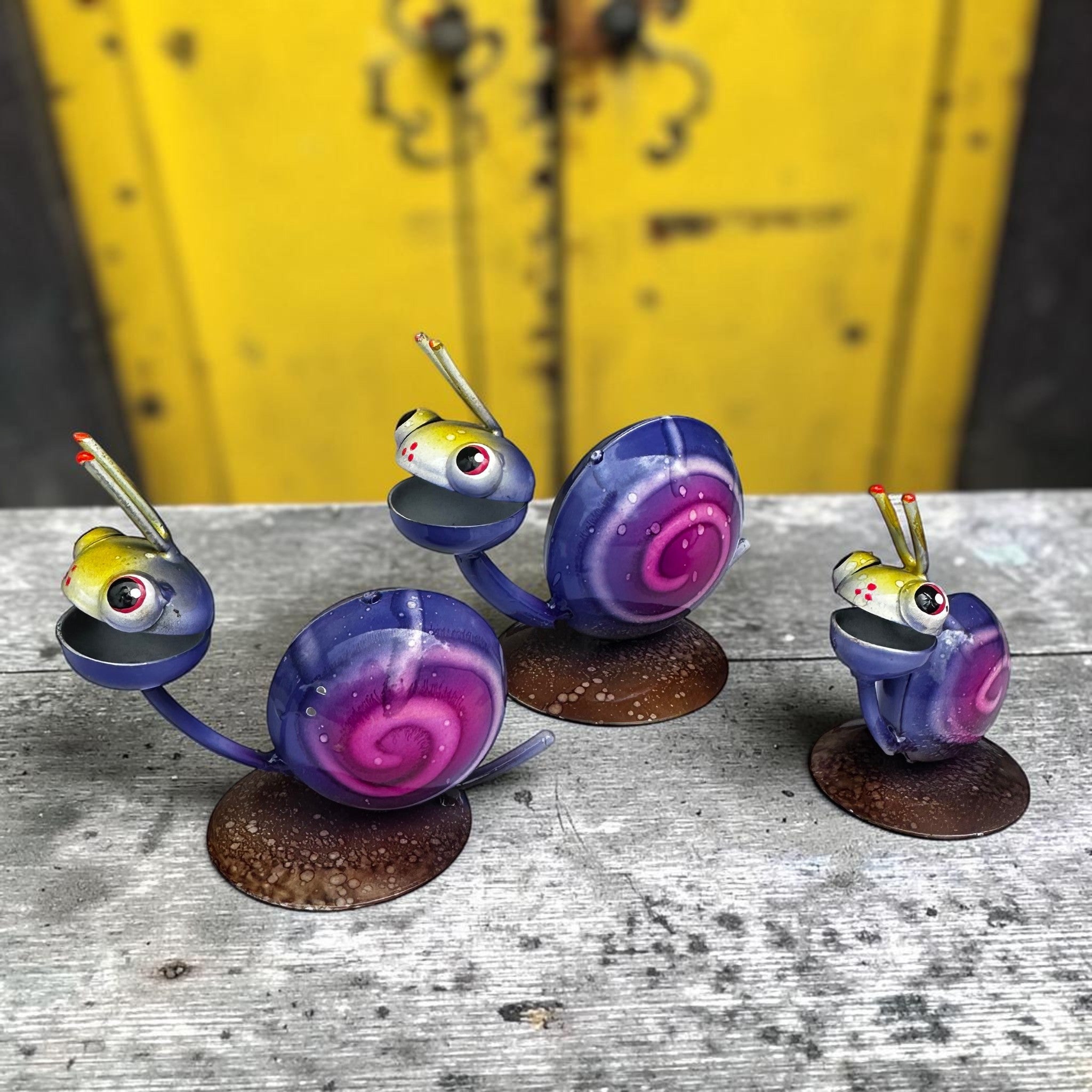 Whimsical Mexican folk art snail trio with purple shells and bright red eyes, hand-painted metal garden sculpture set from Jalisco