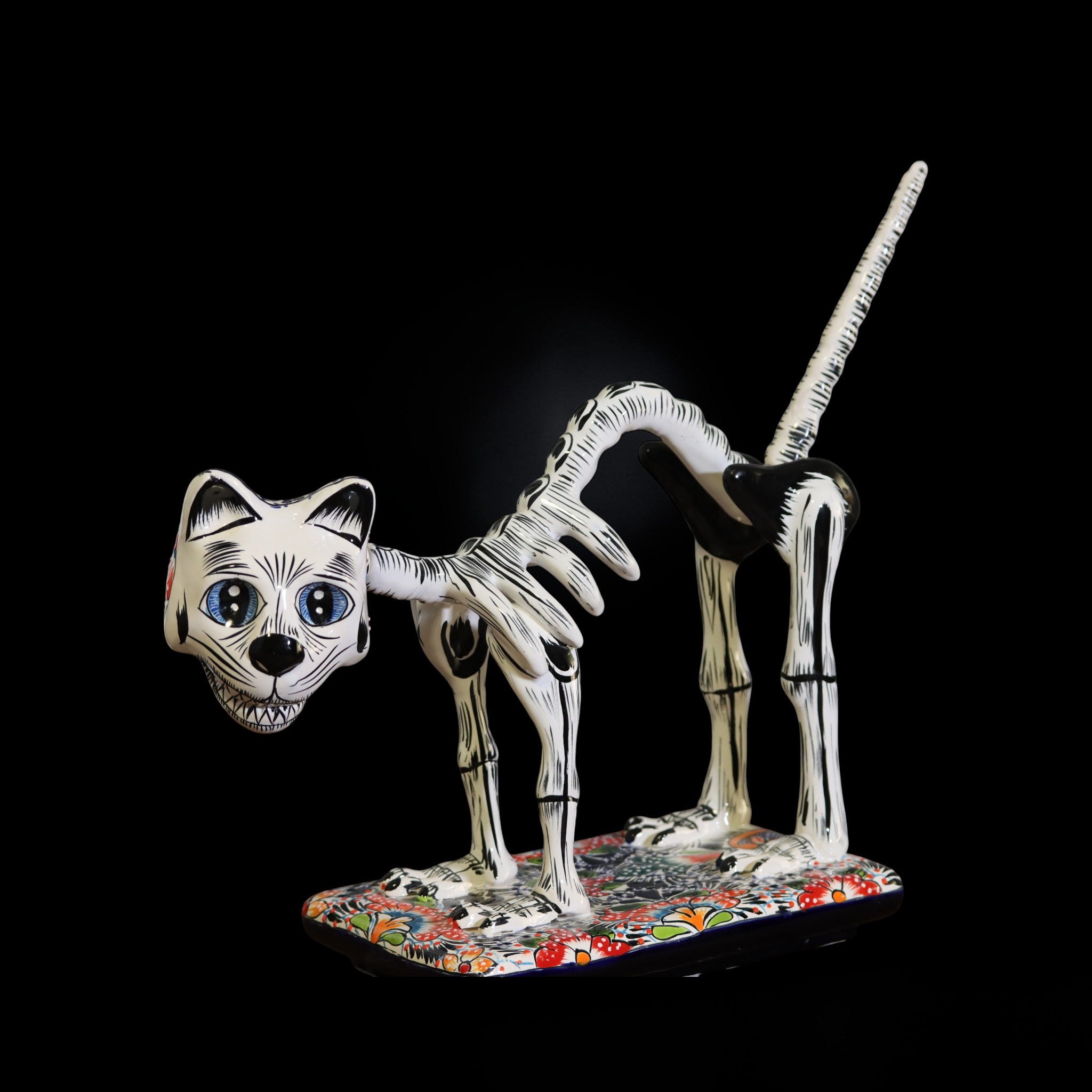 Hand painted Talavera skeletal cat sculpture on colorful base isolated on black background Day of the Dead decor